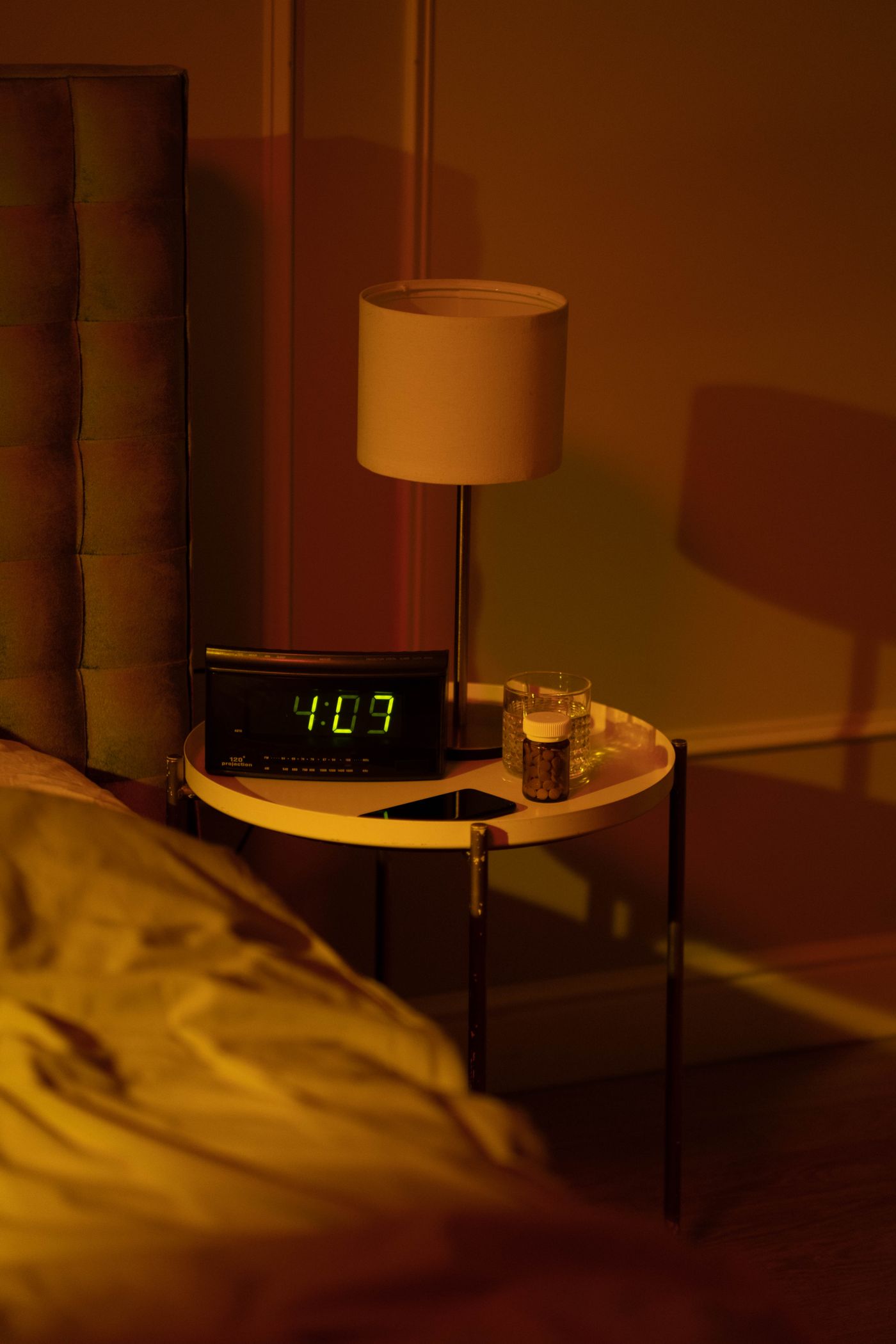 An illuminated digital alarm clock and lamp on a bedside table