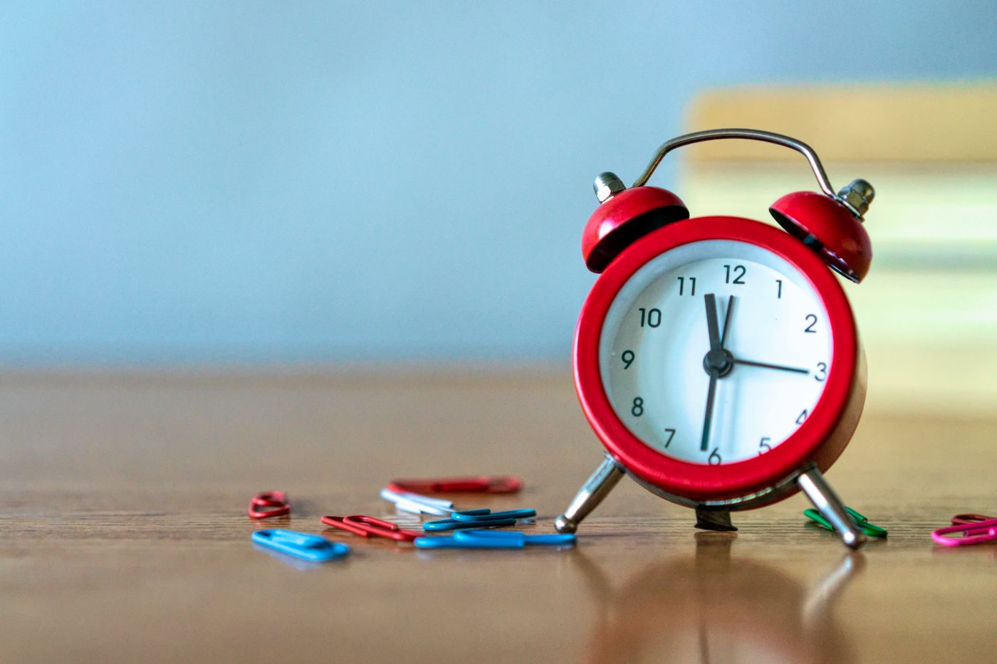 A red desk clock beside paper clips on a work surface