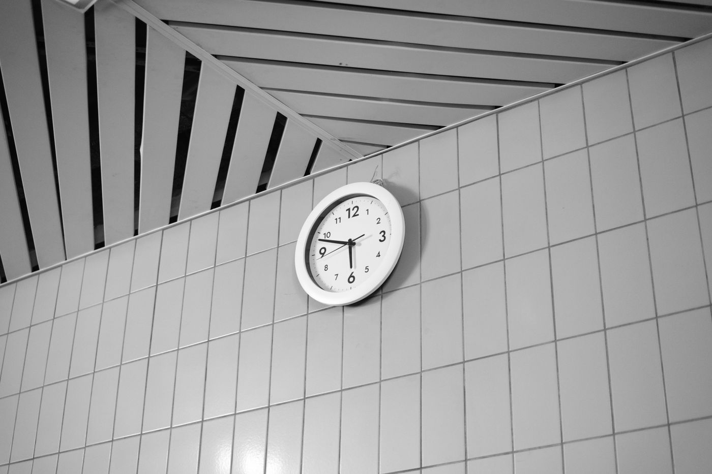 A clearly numbered wall clock mounted high on a tiled wall