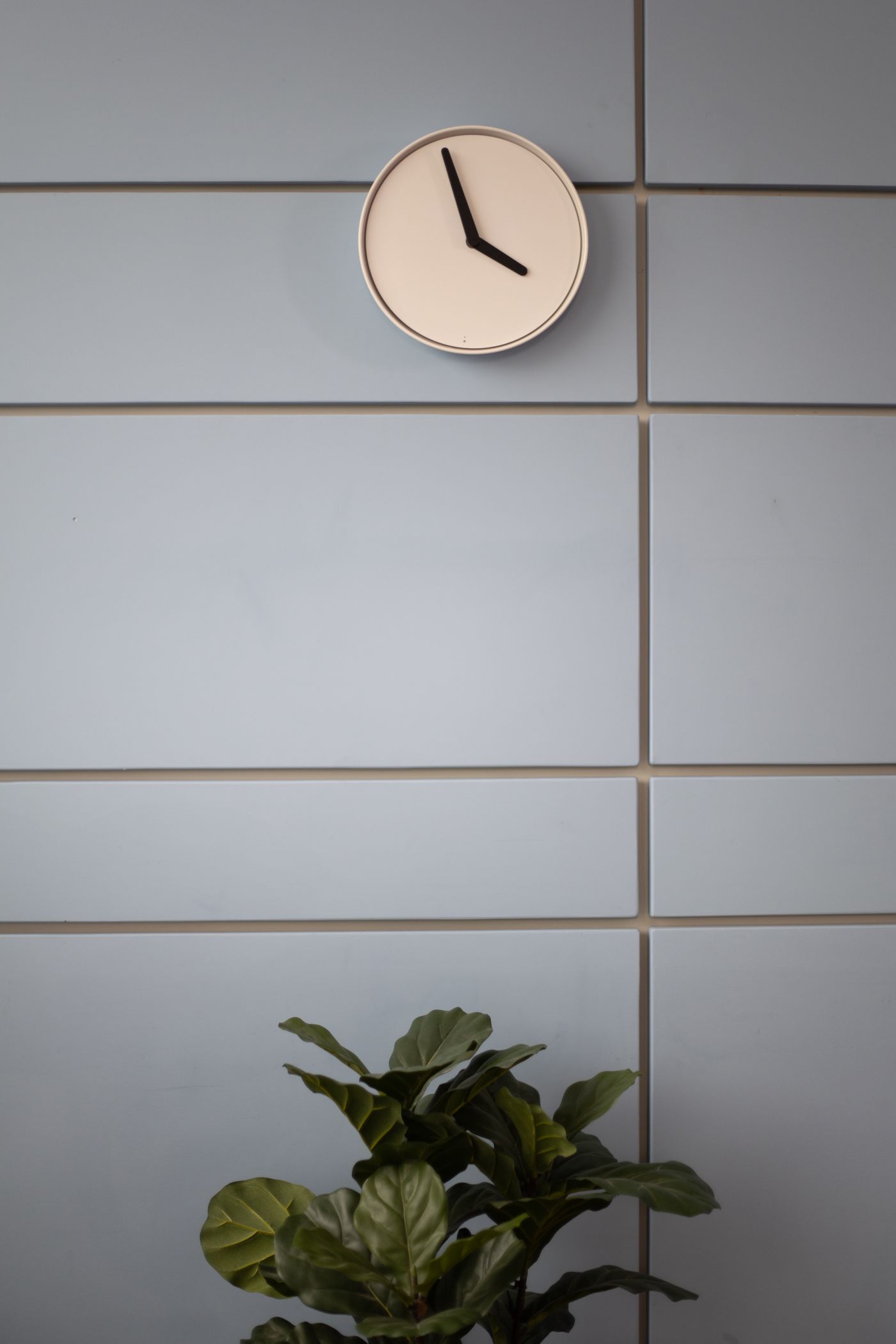 A light wood-rimmed clock against a panelled wall