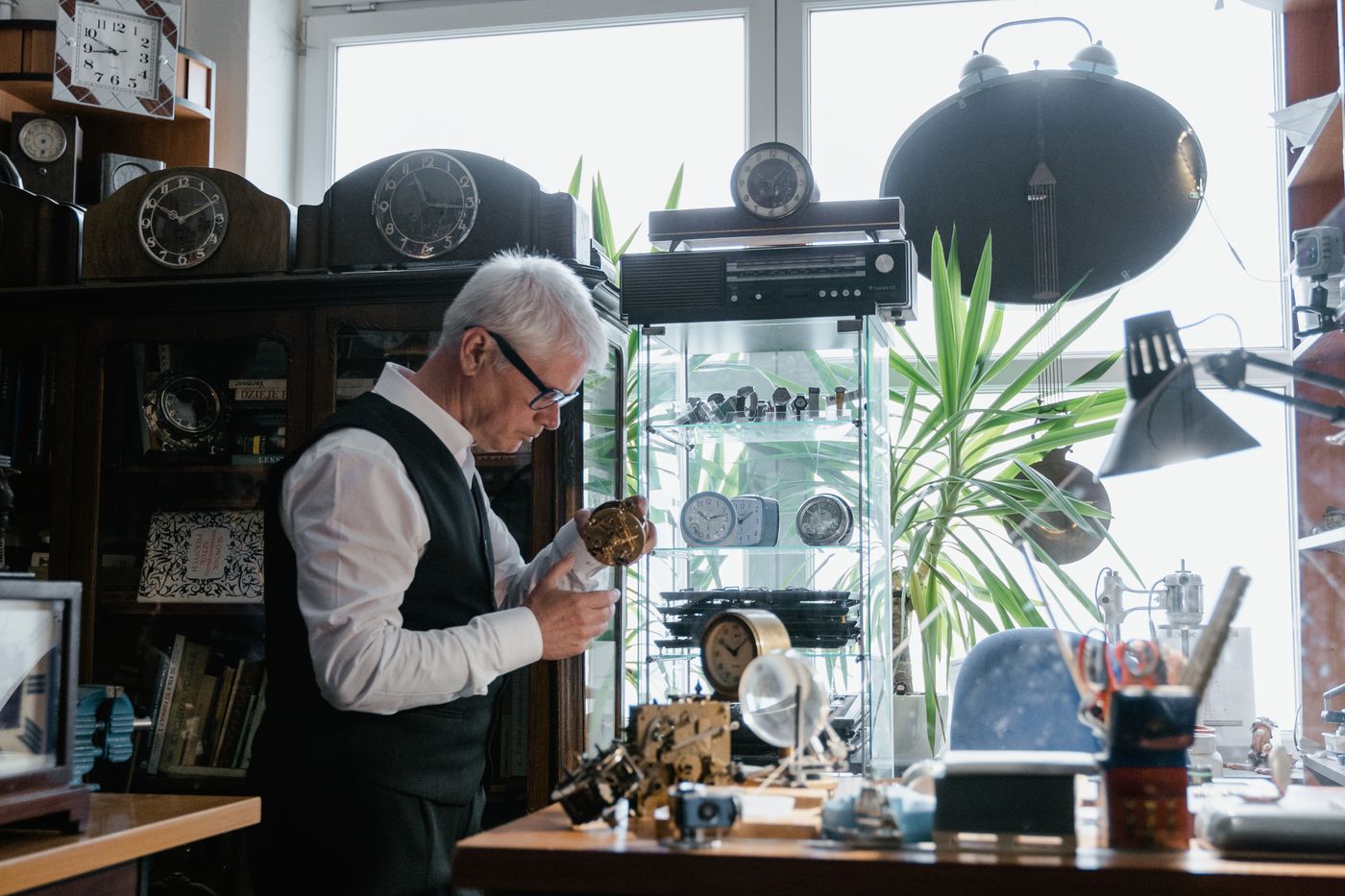 A repairer at a workbench surrounded by clocks and tools