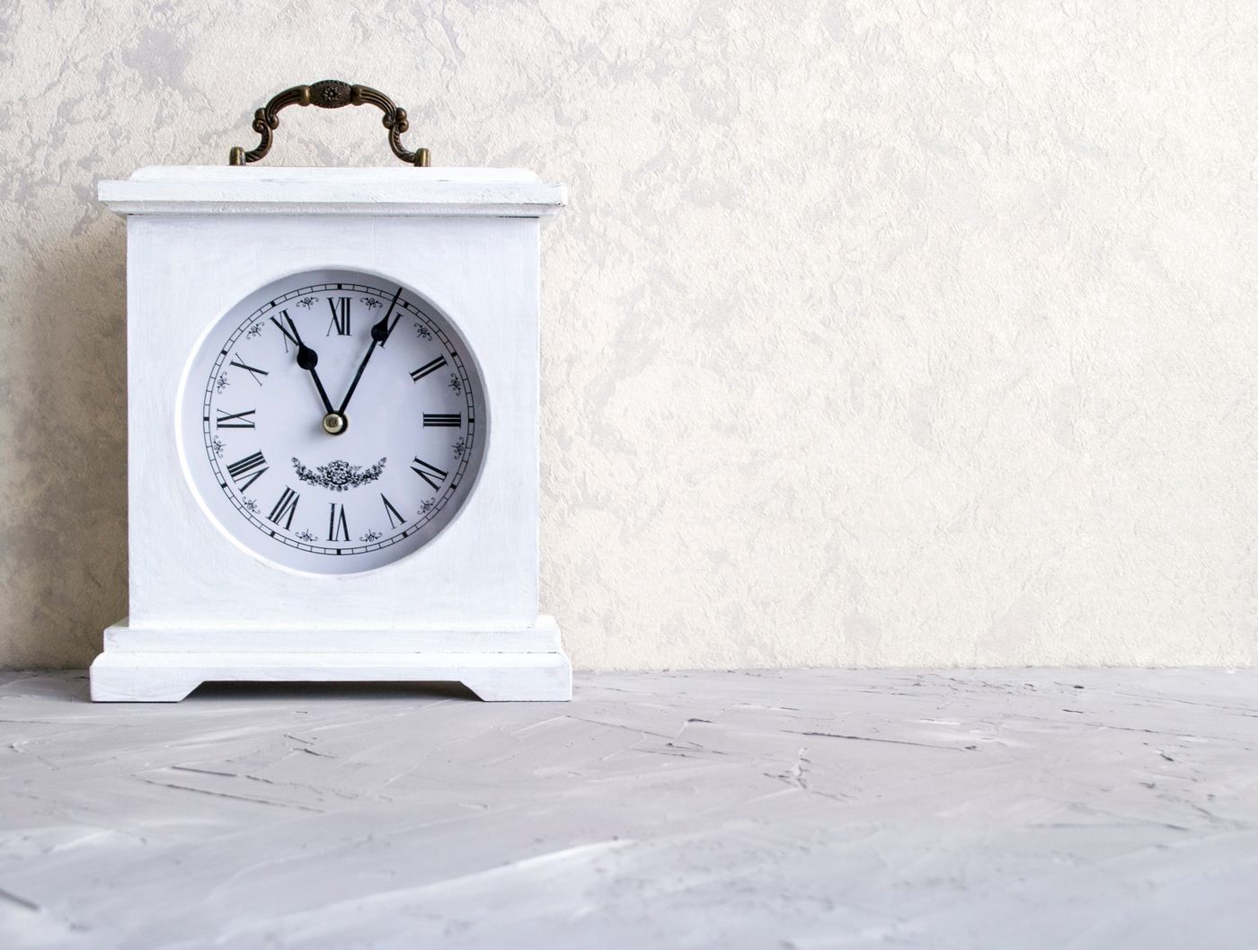 A white mantel clock with Roman numerals and a top handle