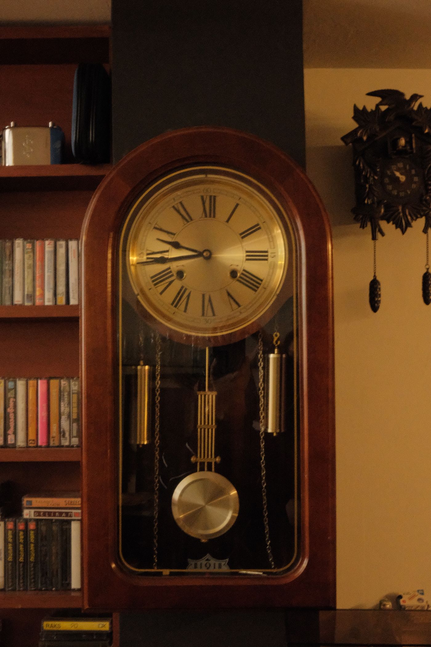 A wooden pendulum wall clock with its pendulum visible behind glass