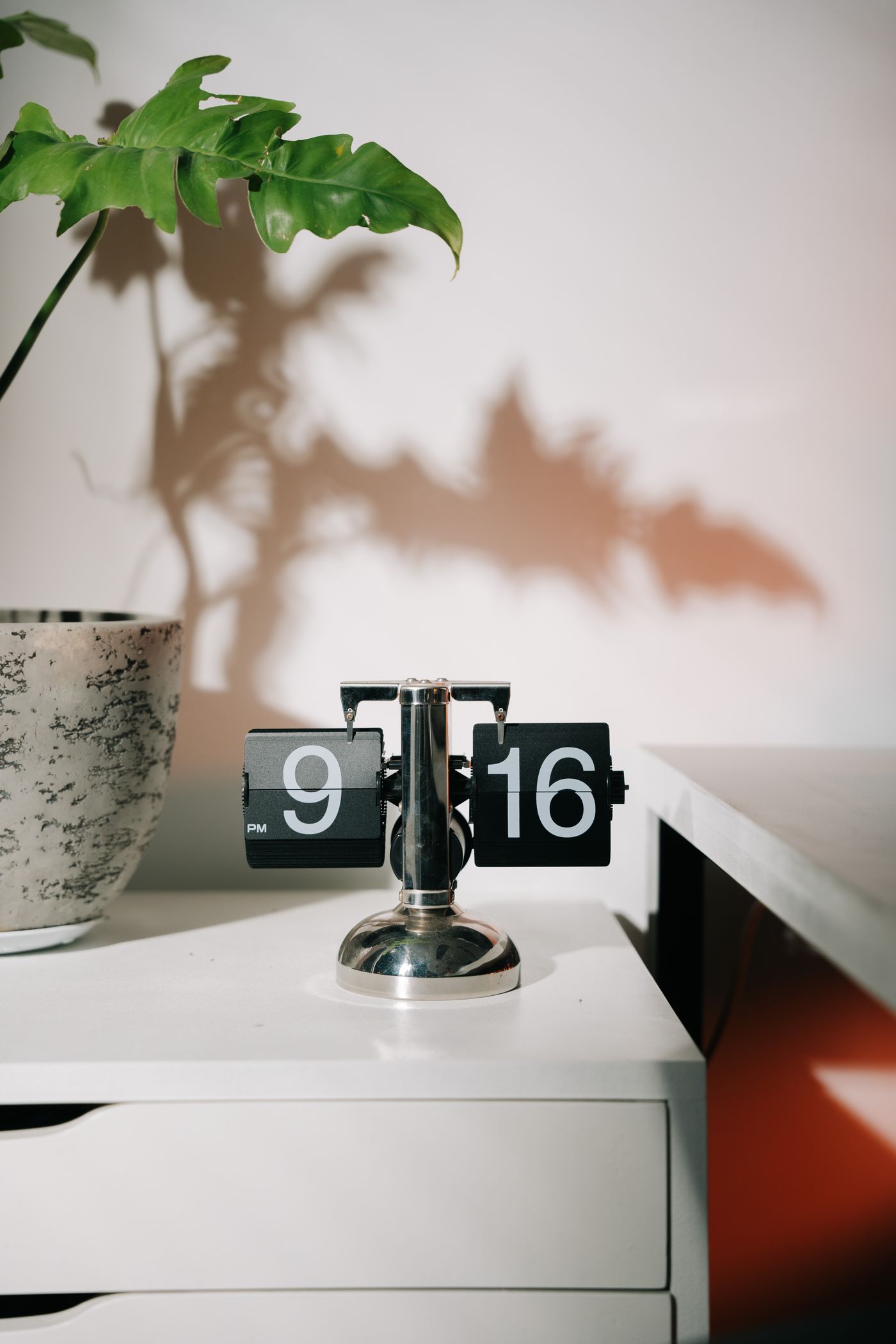 A physical split-flap clock on a tabletop beside a plant