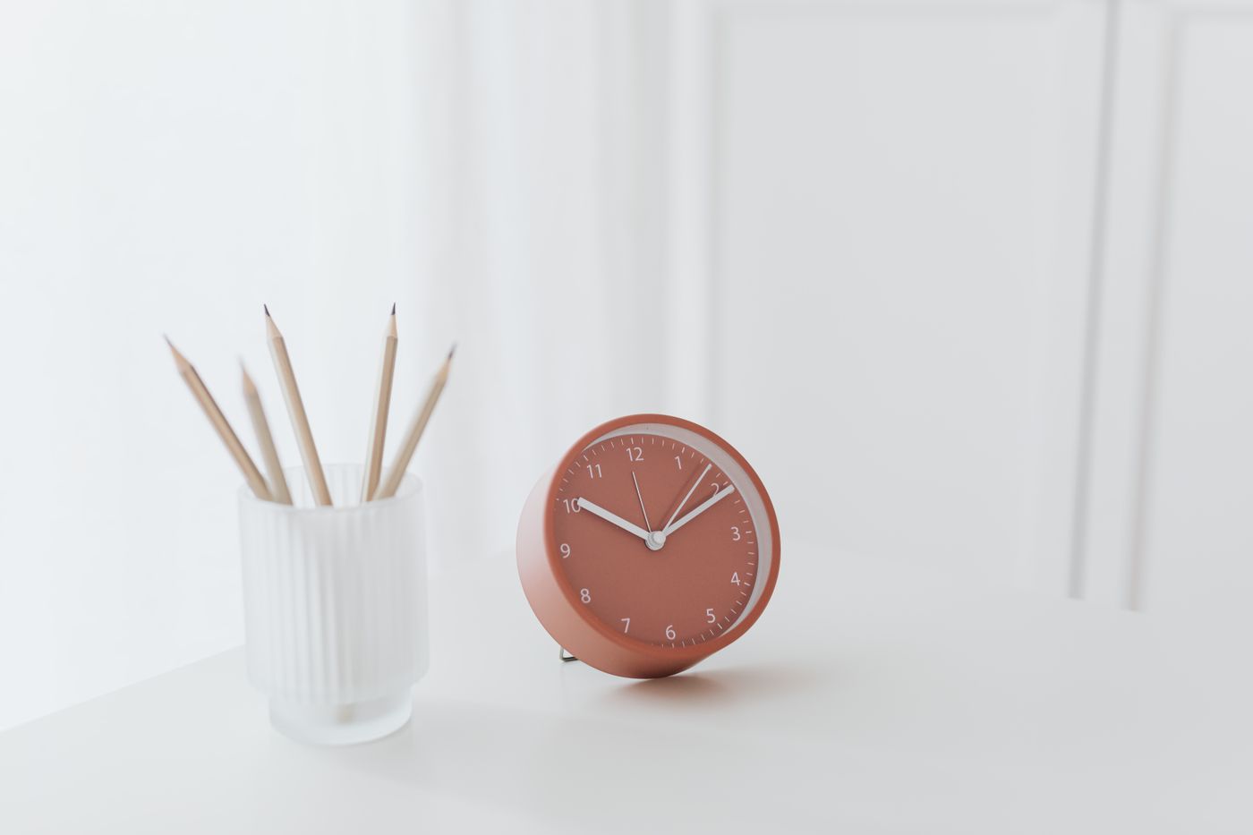 A freestanding red clock on a desk beside a pencil pot