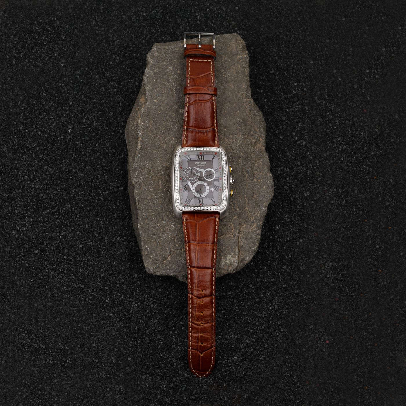A leather watch strap laid out flat with its buckle and holes visible